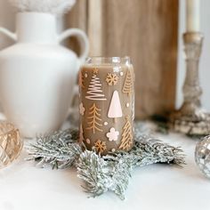 a glass with christmas trees painted on it sitting next to other holiday decorations and candles