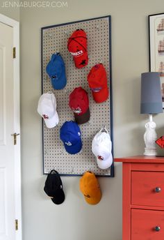 several hats are hanging on a pegboard in the corner of a room next to a dresser