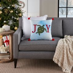 a christmas tree is in the background behind a gray couch with red pom - poms