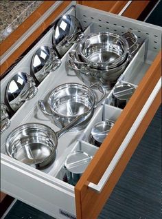 an open drawer in a kitchen filled with stainless steel dishes