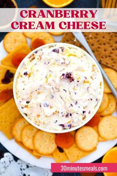 a white plate topped with crackers next to an orange and cranberry cream cheese dip