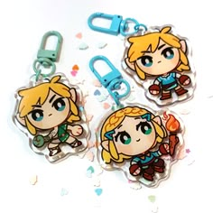 three keychains with cartoon characters on them sitting next to confetti sprinkles