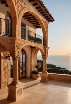 an outdoor patio with stone pillars and arches, overlooking the ocean on a sunny day