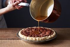 a person pouring caramel sauce on top of a pecan tart crust pie