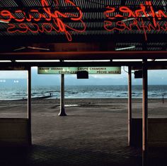 an empty parking lot next to the ocean under a neon sign that reads, future's garbage service