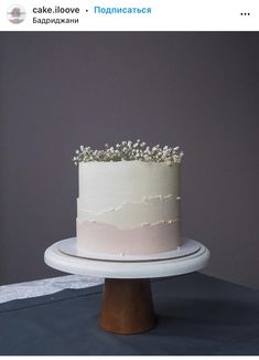 a white and pink cake sitting on top of a wooden table next to a gray wall