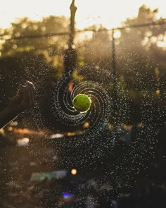 a person holding a tennis ball in their hand while spraying water on the net with it