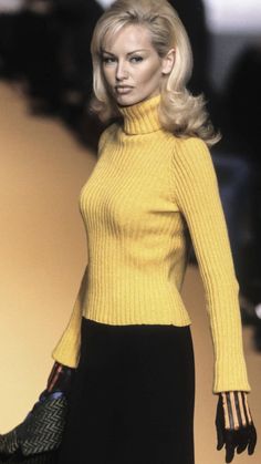 a woman in a yellow turtle neck sweater and black skirt with gloves on the runway