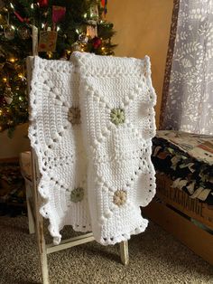 a white crocheted blanket sitting on top of a chair next to a christmas tree