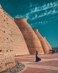 a woman in a long dress standing next to a brick wall and looking at the sky