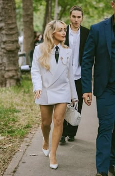 a man and woman walking down a sidewalk next to each other wearing white suits with black ties