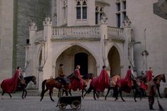 black and white photograph of people in red capes on horses outside an old building