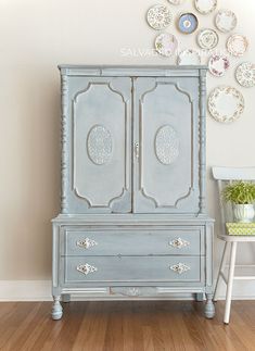 an old dresser painted in blue and white with plates on the wall next to it