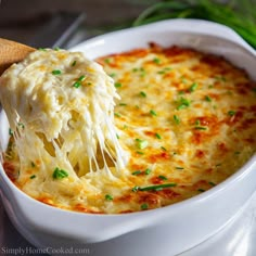 a wooden spoon scooping mashed potatoes from a casserole in a white dish