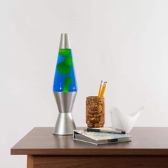 a wooden table topped with a blue and green vase next to a cup filled with pencils