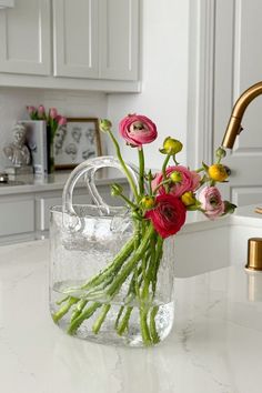 a vase filled with flowers sitting on top of a kitchen counter next to a faucet