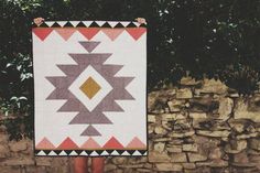 a woman standing next to a stone wall holding a quilt