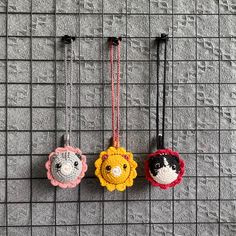 three small crocheted animal ornaments hanging from hooks on a gray wall with black and white squares