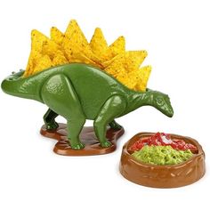 a toy dinosaur next to a bowl of chips and guacamole on a white background