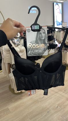 a person holding up a black bra in front of a store display with clothes on it