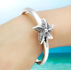 Enhance your jewelry collection with our exquisite Dotted Starfish Bangle, expertly crafted from 925 Sterling Silver. This elegant spring-hinged bracelet combines both style and comfort in a lightweight design that's easy to wear. With an inside circumference of 6.5 inches (16.5 cm), it provides a comfortable fit for most wrists. Each bangle is stamped with '925' to assure you of its sterling silver authenticity. The hollow construction allows for a bold look without the added weight, making it perfect for daily wear or special occasions. Add a touch of marine-inspired charm to your ensemble with this chic and timeless accessory. Satisfaction Guaranteed! Silver Starfish Bracelet For Gift, Silver Starfish Bracelet, Adjustable Silver Starfish Jewelry, Hinged Bracelet, Timeless Accessories, Beach Jewelry, Starfish, Bangle Bracelets, Daily Wear