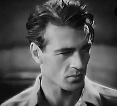 black and white photograph of man with flower in his hair looking at the camera while wearing a shirt