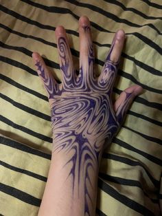 a person's hand with purple and white designs on it sitting on top of a bed