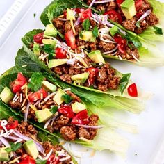 lettuce wraps filled with meat, tomatoes and avocado on a white plate