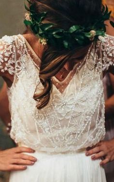 a woman wearing a white dress with greenery in her hair, and holding her hands behind her back