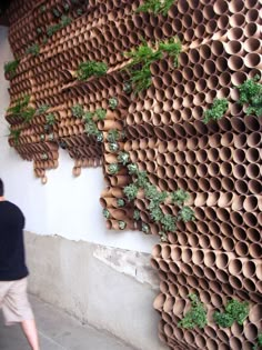 a man walking past a wall made out of clay pipes and plants on the side