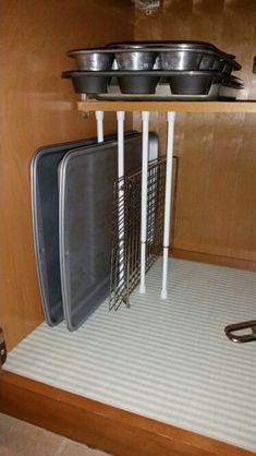 there are many pans and bowls on the shelf in this kitchen cabinet with metal racks