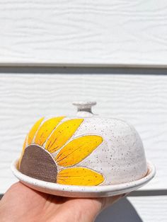 a hand holding a white and yellow flower covered dish