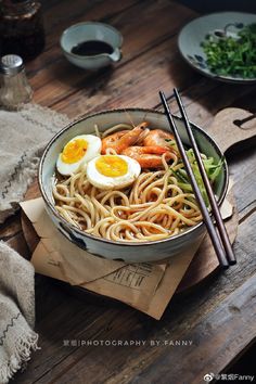 a bowl of noodles with shrimp, eggs and chopsticks on a wooden table