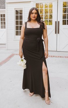 a woman standing in front of a garage wearing a black dress and holding a bouquet