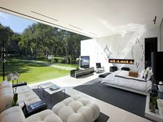 a modern bedroom with white furniture and an open fireplace in the center, overlooking a lush green yard