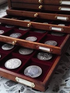 an open wooden box filled with different types of silver and gold coins on top of a marble floor