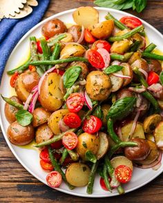 a white plate topped with potatoes, green beans and cherry tomatoes on top of a wooden table