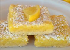 three pieces of lemon bars on a white plate with powdered sugar and two lemon wedges