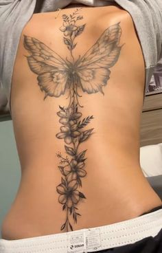 the back of a woman's stomach with flowers and a butterfly tattoo on it