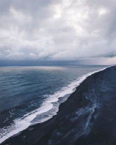 an aerial view of the ocean with waves coming in to shore and dark clouds overhead