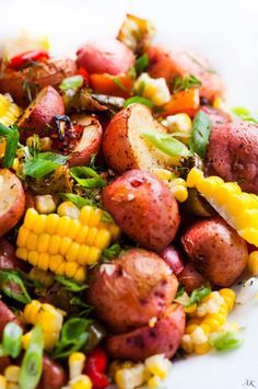 a plate full of potatoes and corn on the cob with green garnish