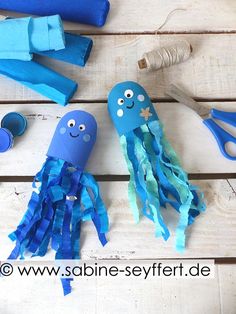 two blue octopus puppets sitting on top of a wooden table next to scissors and yarn