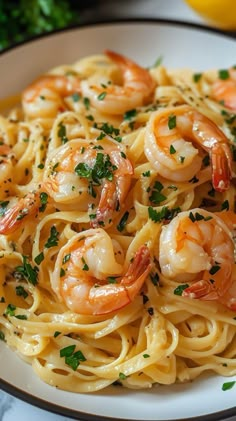 pasta with shrimp and parsley in a white bowl next to lemon wedges on the side