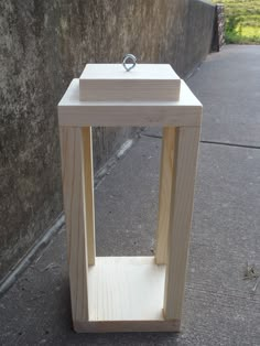 a small wooden table sitting on the sidewalk next to a concrete wall with a ring on it