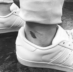 black and white photo of a foot with a small wing tattoo on the left ankle