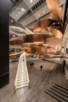 the interior of a large building with stairs and people walking around it in front of an escalator