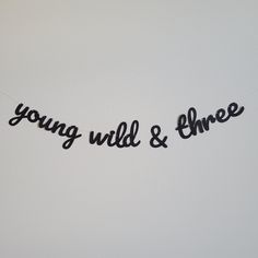 the words young, wild and three are hanging on a white wall with black string