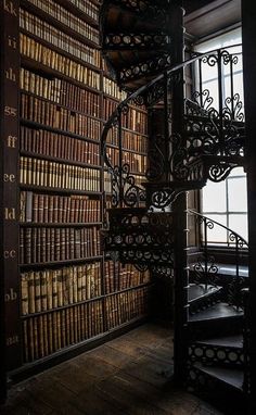 a spiral staircase in front of a bookshelf filled with lots of old books