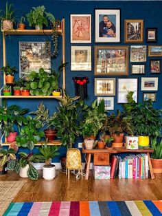 a living room filled with lots of potted plants and pictures on the wall above