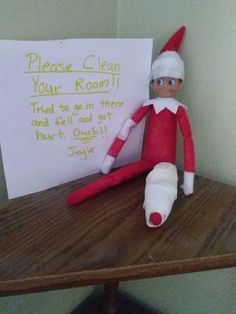 an elf is sitting next to a sign that says please clean your room